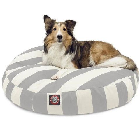 A brown and white collie is lying on the Majestic Pet Vertical Stripe Round Dog Bed, which has gray and white stripes, a removable cover, and a small logo patch on the front.