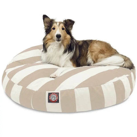 A collie dog lies alert and comfortable on the Majestic Pet Vertical Stripe Round Dog Bed, which has beige and white stripes, a front logo patch, and a washable, removable cover for easy cleaning.