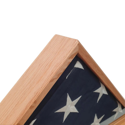 Close-up of the corner of a Legacies of America Woodworking Company Oak Burial Flag Display Case (5 x 9.5) holding a folded American flag with white stars on blue, proudly crafted by veterans against a white background.