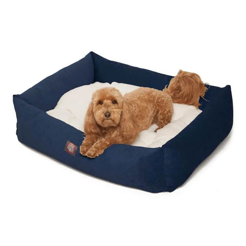 A small, fluffy brown dog is resting on a white cushion inside the Majestic Pet Villa Luxe Bagel Bed, which features dark blue rectangular sides.