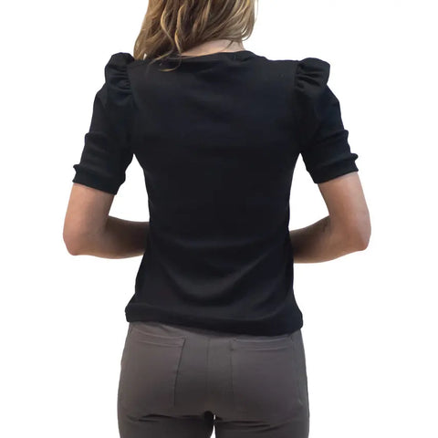A person with long hair is seen from behind wearing the Lamour Top by Spiritex | Sustainable Apparel—a black puffy sleeve blouse—paired with gray pants, set against a plain white background.