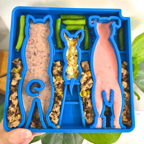 A blue SodaPup Waiting Dogs Design ETray Enrichment Tray for Dogs with dog and rabbit-shaped compartments holds pureed food, chopped veggies, and treats like green beans. Separate sections act as slow feeders for enrichment.