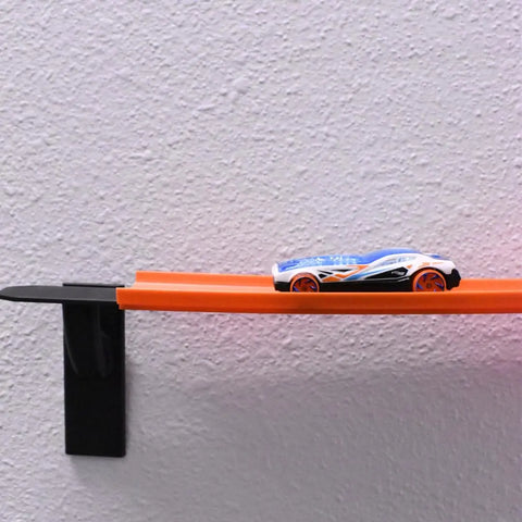 A Hot Wheels-compatible toy race car sits on an orange track mounted horizontally on a textured white wall using Chatelet Manufacturing’s Toy Racetrack Wall Connectors—a fun, Made in USA accessory for kids’ racetrack builds.