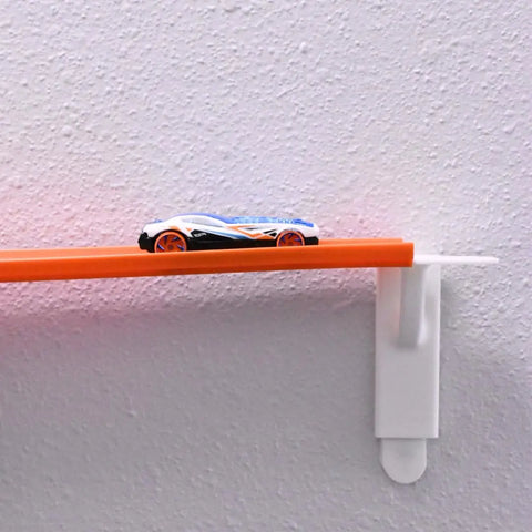 A small race car on an orange track uses Chatelet Manufacturing’s Toy Racetrack Wall Connectors, compatible with Hot Wheels, to race up a textured white wall—fun and easy racetrack building for kids.
