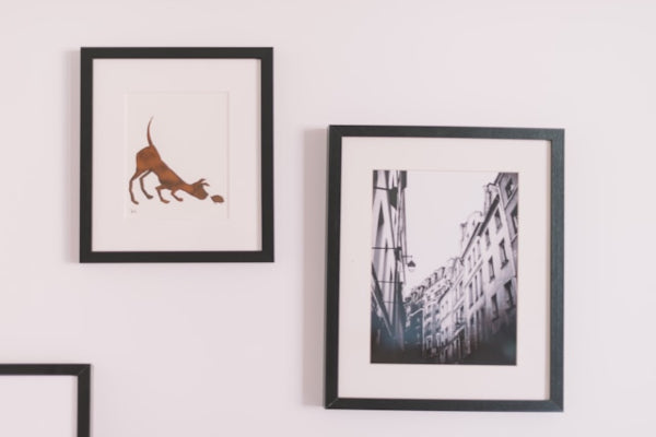 Two framed pictures on a wall, one with a dog illustration and the other with an urban street scene.