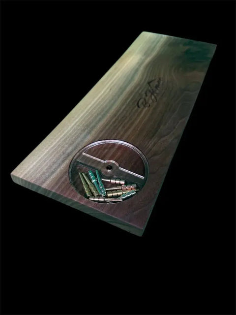 The Walnut Live Edge Cribbage Board by B. James Design & Woodwork is a handcrafted rectangular tray with a recessed circular compartment for built-in peg storage, holding small metal and colored pegs against a black background.