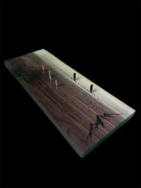 The Walnut Live Edge Cribbage Board by B. James Design & Woodwork features engraved lines, metal pegs with built-in storage, and a mountain design in the corner on a black background, showcasing handcrafted excellence.