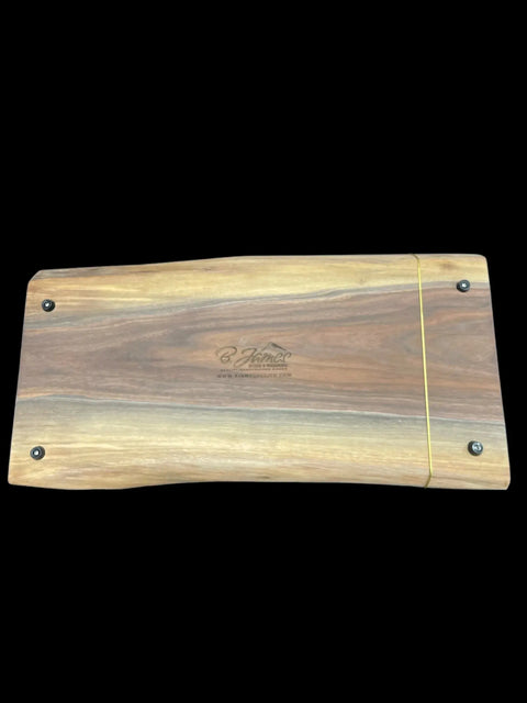 The Walnut Live Edge Serving Tray by B. James Design & Woodwork features a rectangular handcrafted walnut design with rounded edges, visible wood grain, black screws in the corners, a yellow elastic band at one end, and a central engraved logo.