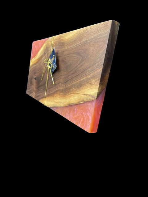 The Sunset Epoxy Walnut Serving Tray by B. James Design & Woodwork features a handcrafted walnut and pink resin design, tied with a yellow ribbon and black tag, shown on a black background. Expertly made in the USA.