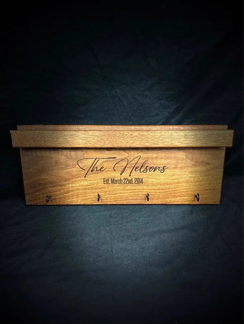 The Sunglasses and Key Rack - Walnut by B. James Design & Woodwork features “The Nelsons Est. March 22nd, 2014” engraved on the front, with four key hooks—a stylish walnut entryway organizer set against a dark background.
