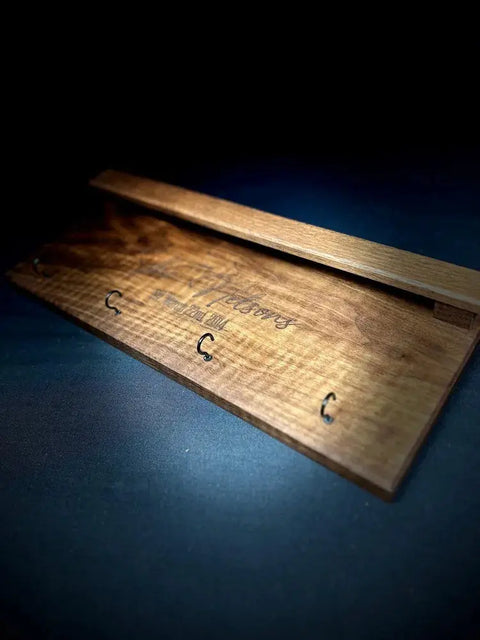 The B. James Design & Woodwork Sunglasses and Key Rack - Walnut features polished walnut wood with subtle engraved text and five metal hooks, ideal for entryway organization, shown against a dark background.