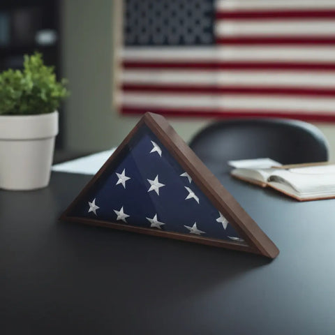 A Legacies of America Woodworking Company Walnut 4x6 Flag Display Case holds a folded flag on a desk beside an open book and potted plant, with a large American flag in the background—proudly Veteran built.