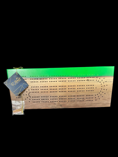 The Lime Green Epoxy Walnut Cribbage Board by B. James Design & Woodwork features multiple scoring holes, a lime green epoxy top edge, and comes with pegs in a small bag attached to the corner. Set against a black background.