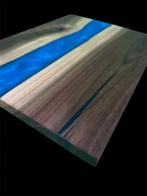 The B. James Design & Woodwork Vivid Blue and Walnut Epoxy Serving Tray features a smooth, handcrafted walnut surface with a striking blue resin river design, showcased here against a black background.
