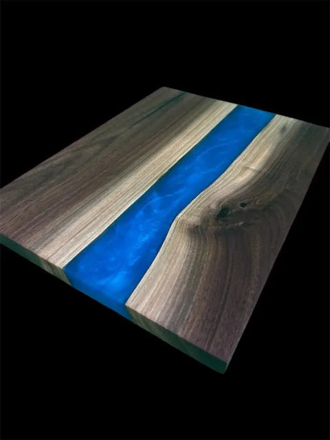The Vivid Blue and Walnut Epoxy Serving Tray by B. James Design & Woodwork features a handcrafted vivid blue resin river flowing through natural walnut wood grain, set against a bold black background for a unique look.