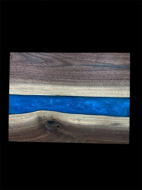 The Vivid Blue and Walnut Epoxy Serving Tray by B. James Design & Woodwork features a striking blue epoxy river through rich walnut, handcrafted for a unique look. The natural wood grain and smooth finish stand out against the black background.