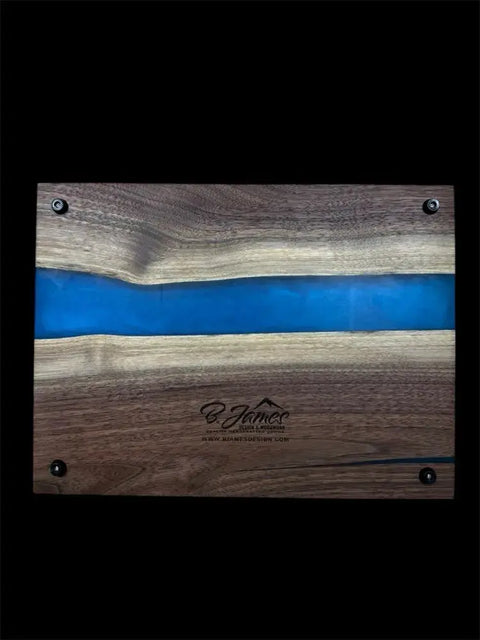 The Vivid Blue and Walnut Epoxy Serving Tray by B. James Design & Woodwork features a unique blue resin river, rectangular shape, visible corner screws, and an engraved logo—showcasing handcrafted quality.