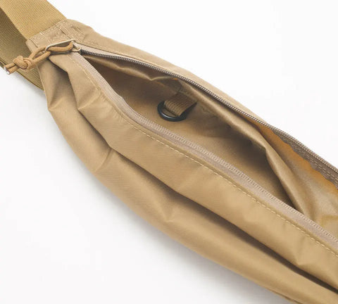A close-up of an open MIS Body Bag - Coyote Tan waist pack, made of packcloth nylon, with a zipper revealing its empty interior and a small black ring on a fabric loop inside.