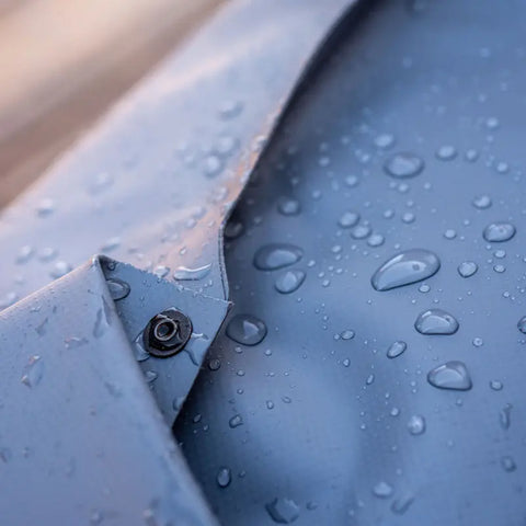 Close-up of the eqpd GearBucket in light blue, showcasing water droplets on its surface that highlight its water-resistant fabric and watertight seams, with a black snap button visible near the collar.