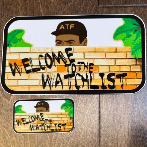 The American Lictor Sticker: Welcome to the Watchlist features a person in an ATF hat peering over a brick wall with WELCOME TO THE WATCHLIST in black, flanked by green bushes, with a smaller matching sticker below.