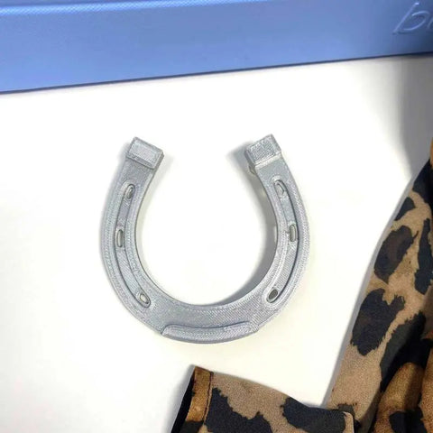 A metallic horseshoe rests on white, partly framed by leopard print fabric, with a blue rectangle behind—ideal inspiration for Chatelet Manufacturings BOGLETS - RODEO Charms: unique decorative tote bag charms made in the USA.