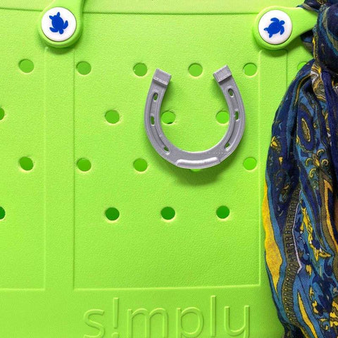 A green surface with round holes displays Chatelet Manufacturings BOGLETS - RODEO Charms, a silver horseshoe, blue and white turtle-designed charms, and a colorful scarf on the right. The word simply appears partially at the bottom.