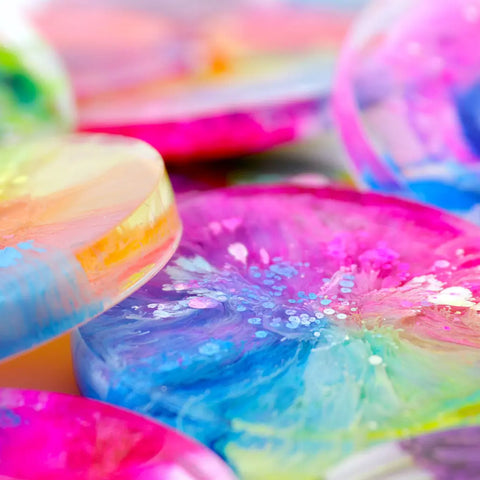Close-up of vibrant petri art coasters with pink, blue, yellow, purple, and white swirls made using ArtResin Alcohol Ink Sinker and epoxy resin for a glossy abstract look.