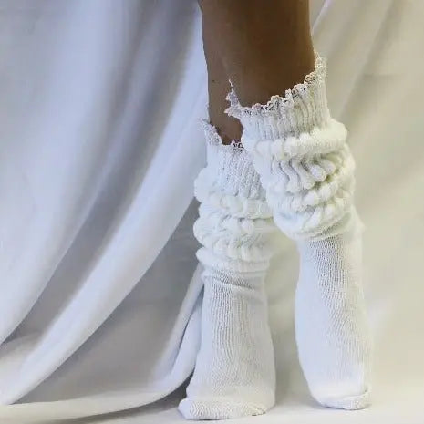 A person wears Catherine Cole’s LACE Topped Ultimate Slouch Socks in white, standing against a white fabric backdrop.