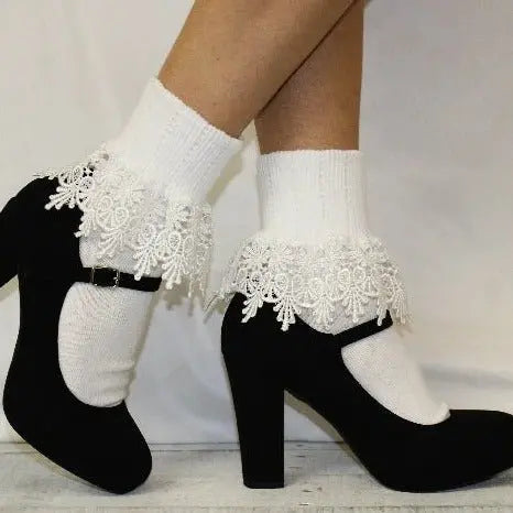 A person stands with one leg crossed over the other against a plain background, wearing black high-heeled Mary Jane shoes paired with Catherine Cole SIGNATURE Lace Cuff Socks in white.