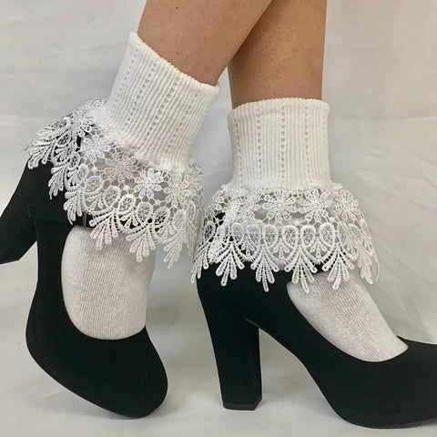 A person wears Catherine Cole SIGNATURE Lace Cuff Socks - White, featuring decorative lace ruffles at the ankle, paired with black Mary Jane heels, shown against a plain white background.