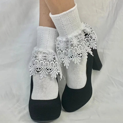 Someone wearing Catherine Cole SIGNATURE Lace Cuff Socks in white stands on a white fabric background, paired with black high-heeled shoes.
