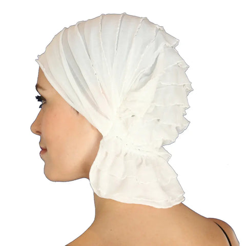 A woman with fair skin is shown in profile, wearing the Chemo Beanies® Stella pleated white slip-on beanie, tied at the back. The plain white background highlights this elegant hair loss headwear by Chemo Beanies®.