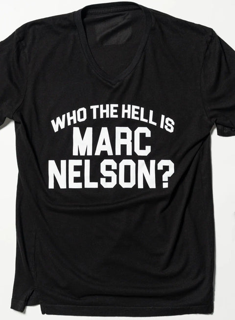 The Who the Hell? Tee by Marc Nelson is a black V-neck, premium cotton T-shirt featuring bold white text, WHO THE HELL IS MARC NELSON?, displayed on a flat white surface.