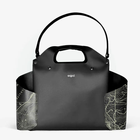 The WideTote - Methow Map by eqpd is a modern black tote with a curved top handle and shoulder strap, featuring white contour map designs on both lower corners and the eqpd logo centered—ideal as a travel organizer bag.