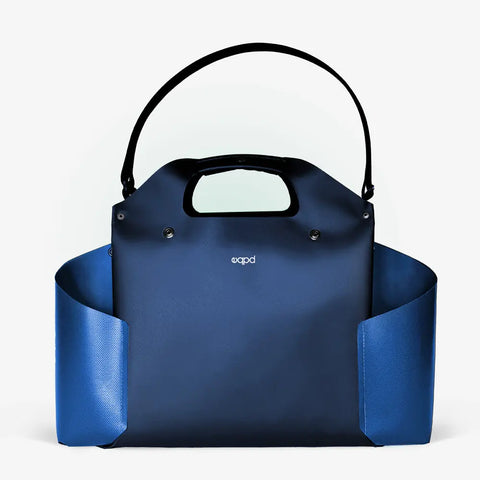 The eqpd WideTote is a modern, structured handbag in dark blue and navy featuring two open side pockets, a short handle, and a detachable shoulder strap—ideal as a travel organizer—shown on a plain white background.