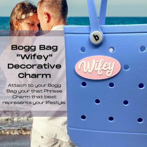 A couple embraces by the water, with a blue Bogg Bag and Chatelet Manufacturings pink and white FRESHe BOGLETS Wifey Charm—decorative accessories compatible with Bogg Bags, Simply Southern, and other totes—showcasing your style.