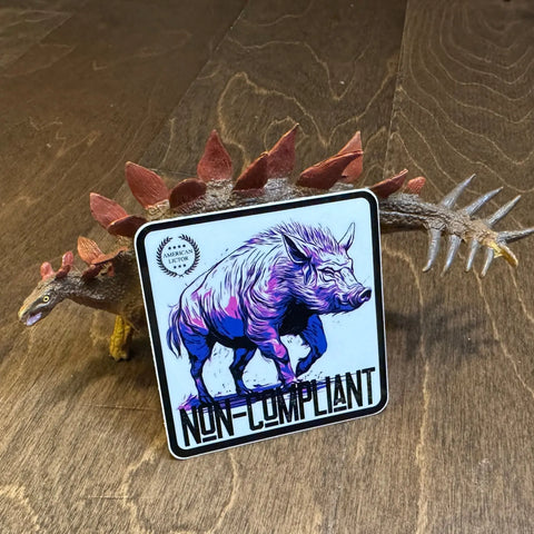 A toy stegosaurus stands on a wooden floor with an American Lictor Sticker: Boar - Non-Compliant in front, displaying a stylized wild boar and the text “Non-Compliant.” The sticker partially covers the dinosaur.