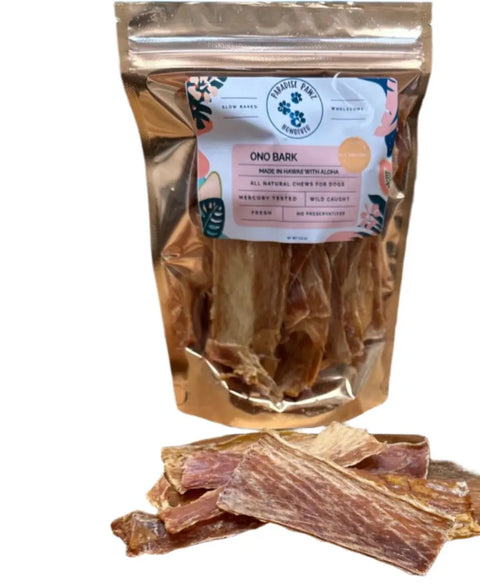 A shiny, resealable Dogtown Bakery Ono Ono Bark bag stands upright, filled with dried fish jerky dog treats. Several pieces of the fish jerky are displayed in front of the package.