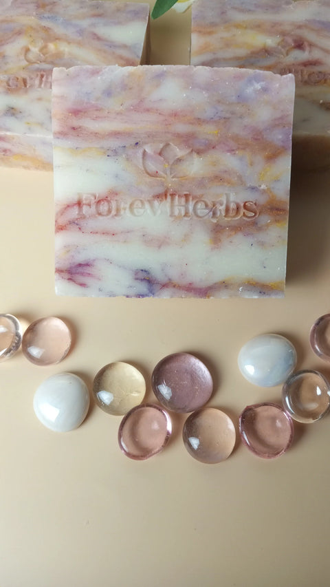 A marbled Wild Orchid Handmade Soap by Forev'Herbs stands upright, featuring embossed branding, and is surrounded by clear and pastel glass pebbles on a light beige surface.