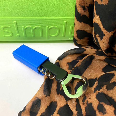 The Chatelet Manufacturing BOGLETS Wine & Bottle Opener Charm Accessory, compatible with Bogg Bags, featuring a black handle and blue cover, is displayed on animal print fabric with a green background and embossed text.