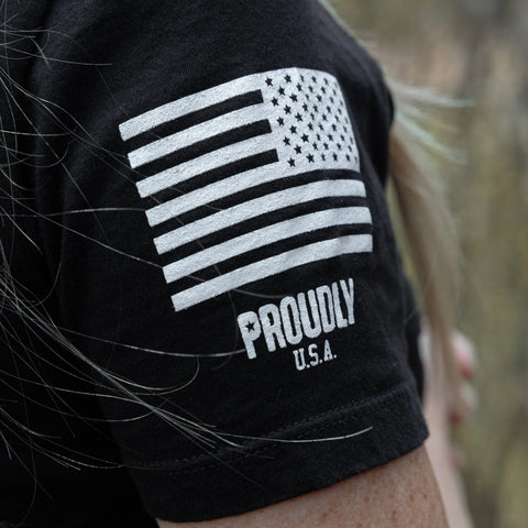 Close-up of a womans arm wearing the Proudly USA American Made Womens Cotton T-Shirt in black, featuring a white American flag and PROUDLY U.S.A. on the sleeve, crafted from 100% combed ring-spun cotton.