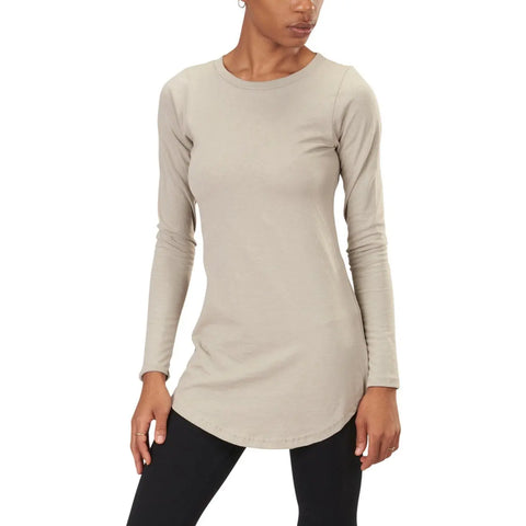 A woman wears the Spiritex Long Sleeve Tunic Tee in light beige, featuring a round neckline, paired with black leggings. She stands against a plain background with one hand on her thigh and the other at her side.