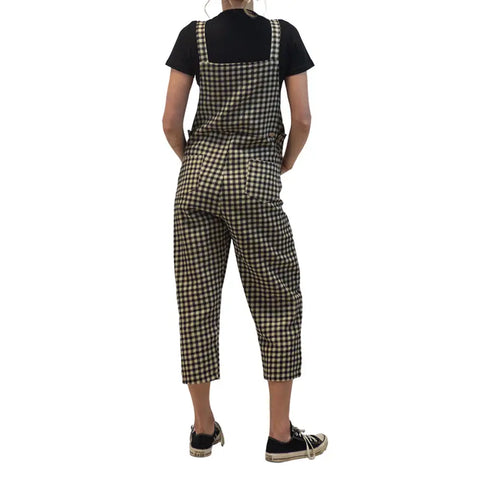 A person faces away from the camera in a Spiritex | Sustainable Apparel Woven Jumper—100% organic cotton, black-and-white checkered, adjustable—paired with a black short-sleeve shirt and black sneakers with white soles against a white backdrop. Made in USA.