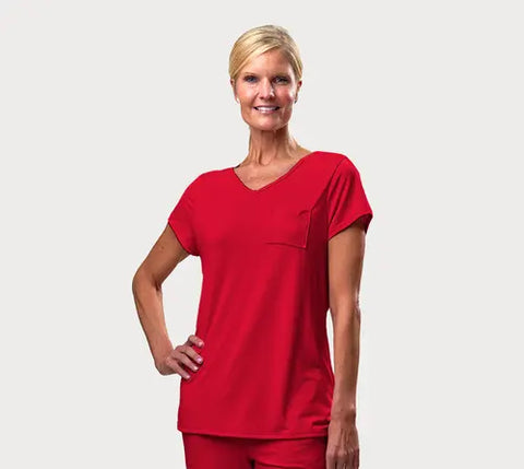 A smiling woman with blonde hair in a low ponytail wears the Goodnighties Short Sleeve V-Neck Tee and matching pants in bright red, standing against a plain light gray background.