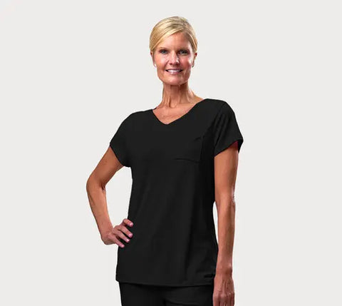 A smiling blond woman in a low bun wears the Goodnighties Short Sleeve V-Neck Tee and matching pants, made from moisture-wicking loungewear fabric, standing confidently with one hand on her hip against a light background.