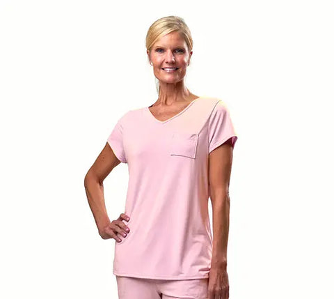A smiling blonde woman with a ponytail wears the Goodnighties Short Sleeve V-Neck Tee in light pink, paired with matching moisture-wicking pants, standing against a plain white background.