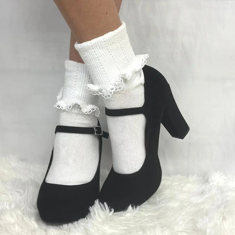 A person wears Catherine Cole SCALLOP Cuff Ankle Socks for women in white and black Mary Jane high heels, standing on a fluffy white surface against a plain white background.