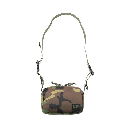 The MIS AW Shoulder Bag S in Woodland Camo is a compact packcloth nylon bag with an adjustable strap, black plastic buckles, an MIS patch on the lower right corner, and is proudly made in the USA.