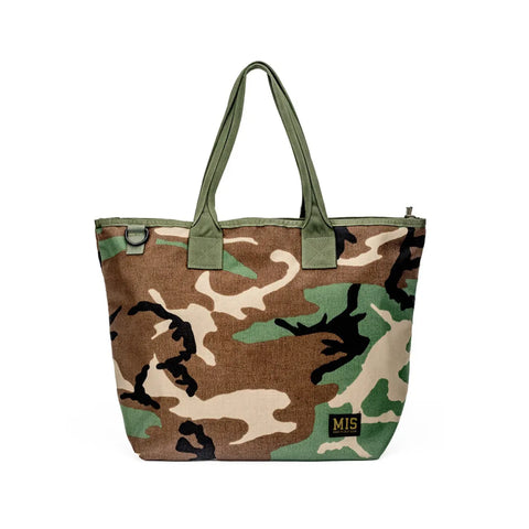 The MIS Tote Bag - Woodland Camo features durable Cordura nylon in a camouflage pattern, two green handles, and a yellow MIS logo patch. This water-resistant tote combines style and function for everyday use.