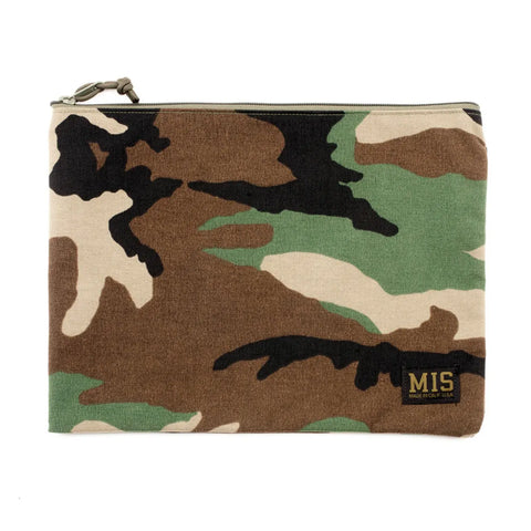The MIS Tool Pouch L - Woodland Camo is a rectangular, zippered pouch with a green, brown, beige, and black camouflage pattern. Made in the USA from water-resistant Cordura nylon, it features a small black MIS patch with yellow lettering.